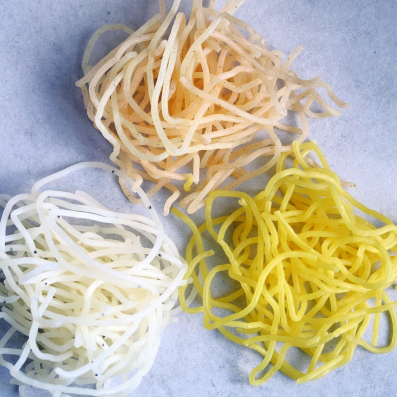 May include: Three piles of thin, dried noodles. One pile is white, one is yellow, and one is a light beige color.