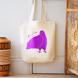 May include: A white canvas tote bag with a purple pigeon illustration and the word "Pijin" printed on it.