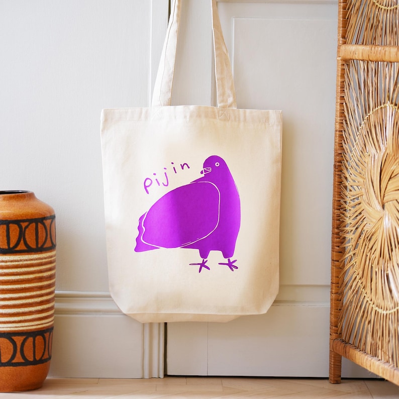 May include: A white canvas tote bag with a purple pigeon illustration and the word "Pijin" printed on it.