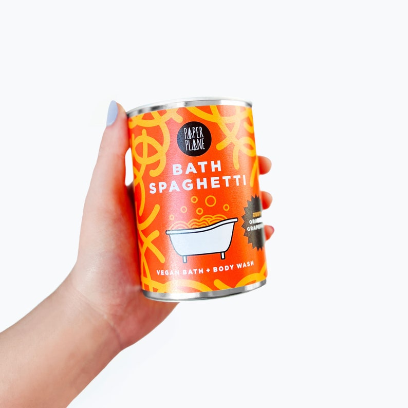 May include: Orange and white can of vegan bath and body wash with the text "Bath Spaghetti" and "Paper Plane" on the front. The can has a graphic of a bathtub with noodles in it.