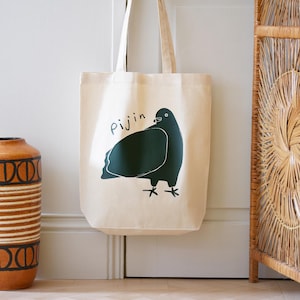 May include: A beige canvas tote bag with a green illustration of a pigeon and the word "Pijjin" printed on the front.