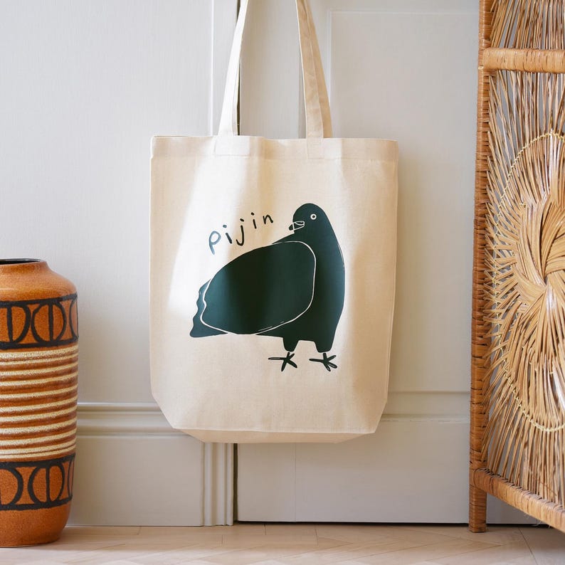 May include: A beige canvas tote bag with a green illustration of a pigeon and the word "Pijjin" printed on the front.