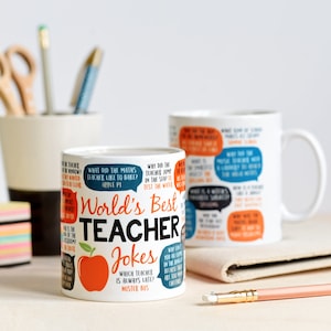 Könnte beinhalten: Zwei weiße Keramikbecher mit einem schwarzen und orangefarbenen Design. Die Becher zeigen eine Vielzahl von Lehrerwitzen, die darauf gedruckt sind. Der Text auf einem Becher lautet "World's Best Teacher Jokes".