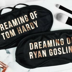 Puede incluir: Dos antifaces negros con letras doradas. El primer antifaz dice "Dreaming of Tom Hardy" y el segundo antifaz dice "Dreaming of Ryan Gosling".