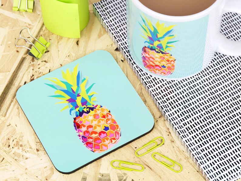 May include: A turquoise blue coaster with a colorful geometric pineapple design. The pineapple is made up of yellow, orange, pink, red, blue, and green colors.