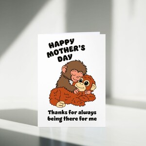 May include: A white Mother's Day greeting card featuring a cartoon illustration of two monkeys hugging. The text "Happy Mother's Day" is at the top, with "Thanks for always being there for me" at the bottom.