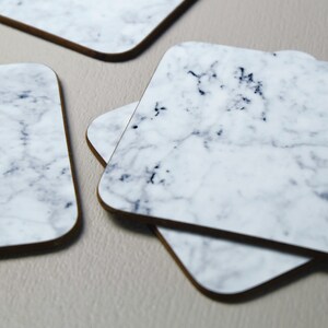 May include: Four square white marble coasters with a grey veining pattern. The coasters are stacked on top of each other.