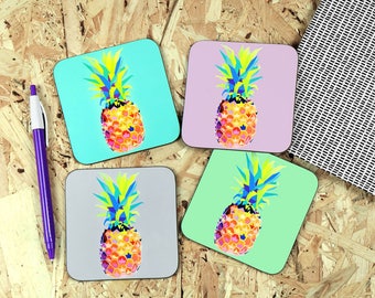 May include: Four square coasters with a geometric pineapple design. The pineapples are in shades of yellow, orange, blue, and green. The coasters are on a wood background.