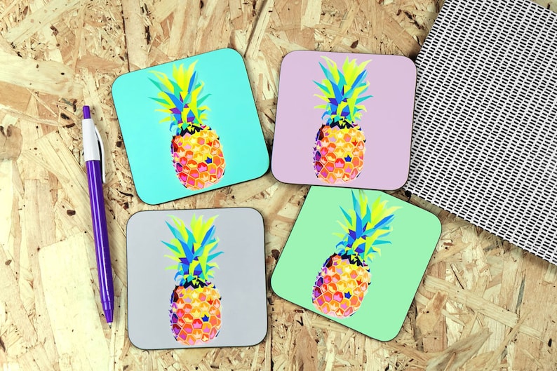 May include: Four square coasters with a geometric pineapple design. The pineapples are in shades of yellow, orange, blue, and green. The coasters are on a wood background.