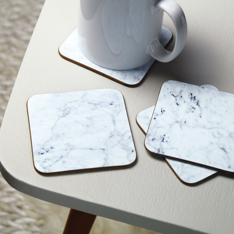 May include: Four square white coasters with a marble pattern. The coasters are made of cork and have a brown border.