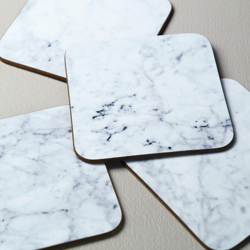 May include: Four white marble coasters with a gray veining pattern. The coasters are square and have a cork backing.