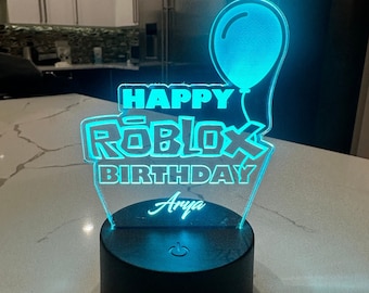 May include: A blue and white LED night light with the words "Happy Roblox Birthday" and the name "Arya" on it. The light is shaped like a balloon and has a switch on the base.