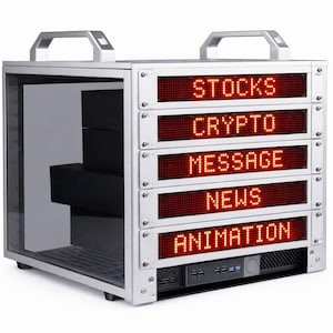 Op de afbeelding: Een zilverkleurige elektronische display case met een handvat aan de bovenkant. Het display toont de woorden "STOCKS", "CRYPTO", "MESSAGE", "NEWS" en "ANIMATION" in rode LED-verlichting. Binnenin de case bevinden zich zwarte dozen.