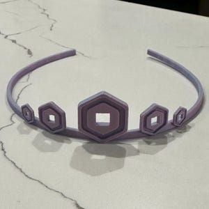 May include: A lavender crown with a series of geometric shapes. The crown features a central, larger hexagon with a square cutout, flanked by smaller, similar shapes. The headband is a gradient of lavender and light blue.