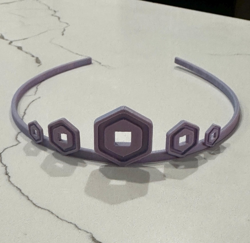 May include: A lavender crown with a series of geometric shapes. The crown features a central, larger hexagon with a square cutout, flanked by smaller, similar shapes. The headband is a gradient of lavender and light blue.