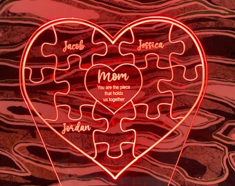 May include: A heart-shaped LED night light with a puzzle design. The light is red and features the names "Jacob", "Jessica", and "Jordan". The word "Mom" is in the center, with the text "You are the piece that holds us together".