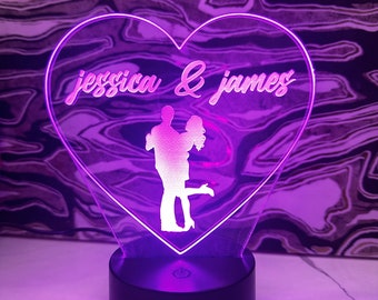 May include: A heart-shaped LED night light with a silhouette of a couple embracing. The light is purple and the text "jessica & james" is engraved on the front.