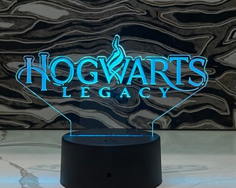 May include: A blue and white LED light with a diamond-shaped base. The light features the Hogwarts Legacy logo with a stylized flame design.