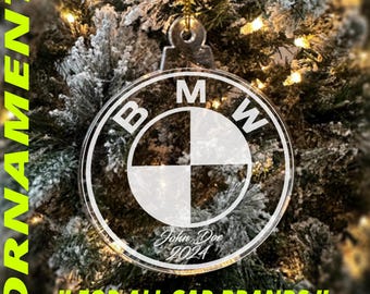 May include: A clear round Christmas ornament with a white BMW logo and the text "John Doe 2024".