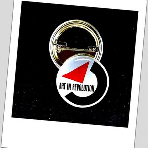 Könnte beinhalten: Ein schwarz-weißer Knopf mit einem roten Dreieck und dem Text "Art in Revolution".