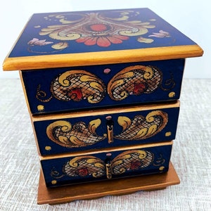 May include: A wooden jewelry box with three drawers. The box is painted blue with gold trim and intricate floral designs in red, yellow, and gold.
