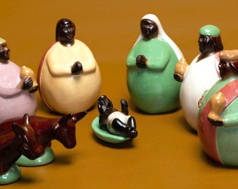 May include: A nativity scene set with seven ceramic figurines. The figures are painted in various colors, including green, pink, red, and yellow. The figures are arranged in a circle around a small, brown ceramic figure of a baby.