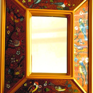 May include: A rectangular gold-framed mirror with a decorative border. The border features a dark red background with colorful birds and floral designs. The mirror's frame has a gold finish, adding a touch of elegance.