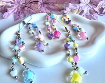 May include: Three colorful beaded charms with heart and round beads in pastel colors. Each charm has a silver-tone metal clasp and a clear heart-shaped bead at the bottom. The charms are displayed on a white, wavy dish.