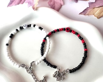 May include: Two beaded bracelets. One bracelet features black and white beads with heart-shaped beads. The other bracelet has black, red, and white beads with a heart-shaped bead. Both bracelets have silver-colored chain clasps.