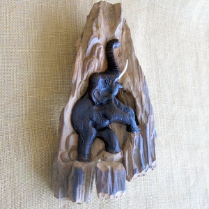 K&ouml;nnte beinhalten: Eine Wandskulptur aus Holz eines Elefanten, der in ein St&uuml;ck Treibholz geschnitzt ist. Der Elefant ist schwarz und das Holz ist braun.