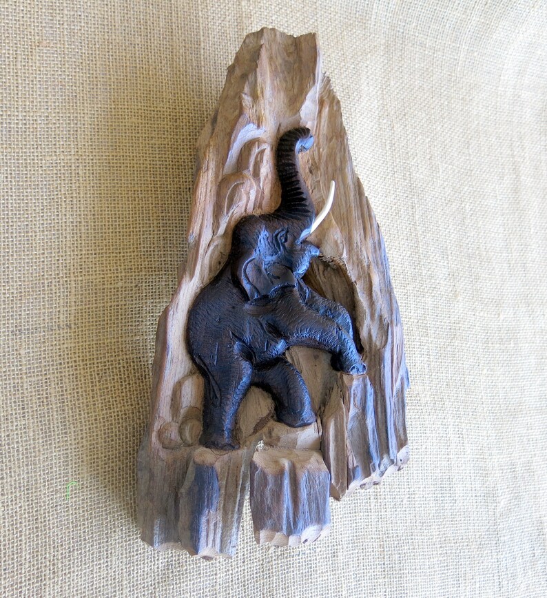 K&ouml;nnte beinhalten: Eine Wandskulptur aus Holz eines Elefanten, der in ein St&uuml;ck Treibholz geschnitzt ist. Der Elefant ist schwarz und das Holz ist braun.