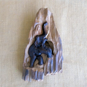 K&ouml;nnte beinhalten: Eine geschnitzte Elefantenfigur aus Holz mit erhobenem R&uuml;ssel und Sto&szlig;z&auml;hnen. Der Elefant ist auf einem St&uuml;ck Treibholz mit nat&uuml;rlicher Holzmaserung montiert.