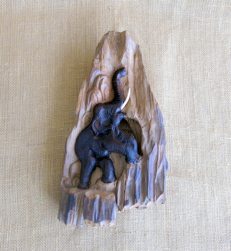 K&ouml;nnte beinhalten: Eine geschnitzte Elefantenfigur aus Holz mit erhobenem R&uuml;ssel und Sto&szlig;z&auml;hnen. Der Elefant ist auf einem St&uuml;ck Treibholz mit nat&uuml;rlicher Holzmaserung montiert.