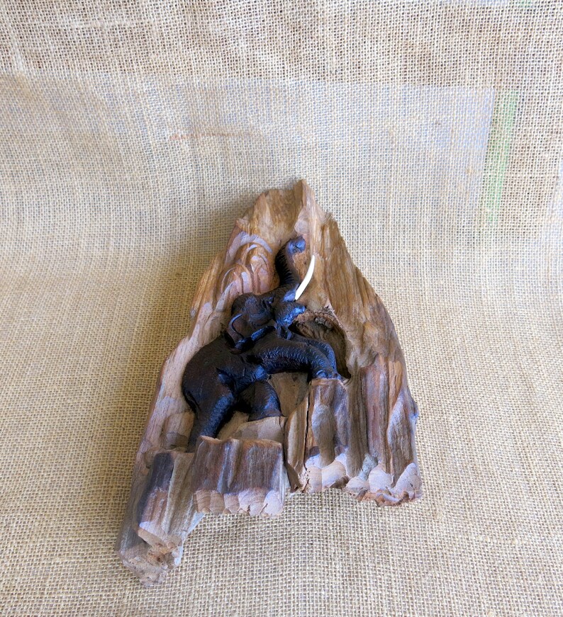 K&ouml;nnte beinhalten: Eine geschnitzte Holzskulptur eines Elefanten mit einem einzigen Sto&szlig;zahn, vor einem Hintergrund aus Naturholz.