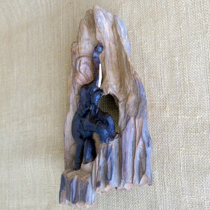 K&ouml;nnte beinhalten: Eine Holzskulptur eines Elefanten mit erhobenem R&uuml;ssel, geschnitzt in ein St&uuml;ck Treibholz. Der Elefant ist schwarz und das Holz ist braun.