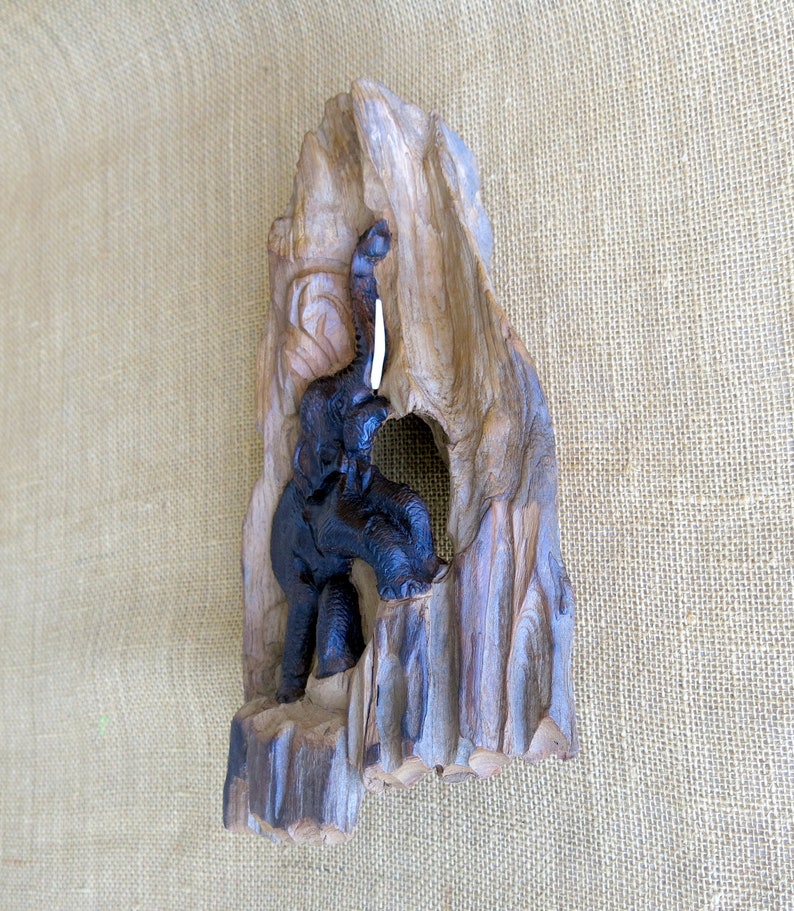 K&ouml;nnte beinhalten: Eine Holzskulptur eines Elefanten mit erhobenem R&uuml;ssel, geschnitzt in ein St&uuml;ck Treibholz. Der Elefant ist schwarz und das Holz ist braun.