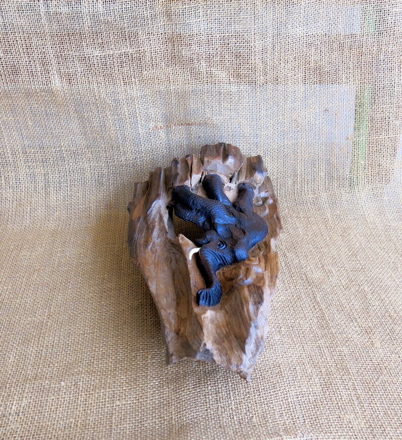 K&ouml;nnte beinhalten: Eine geschnitzte Elefantenfigur aus Holz mit dunkelbrauner Oberfl&auml;che, eingebettet in ein St&uuml;ck Treibholz mit nat&uuml;rlicher Holzmaserung.