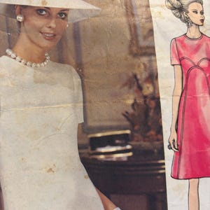 May include: Vintage image featuring a woman in a white dress, hat, and gloves, adorned with pearls. The hat has a black band. A fashion illustration of a pink dress is on the right. The image has a retro aesthetic.