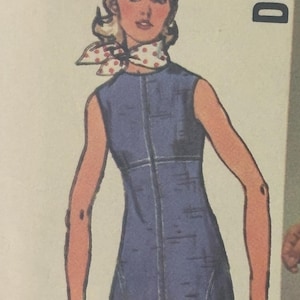 Könnte beinhalten: Eine Vintage-Schnittmuster-Illustration zeigt ein ärmelloses blaues Kleid mit einer vorderen Mittelnaht und zwei Seitentaschen. Die Figur trägt ein weißes Halstuch mit roten Punkten und ein rotes Armband. Der Text DESI ist in der Ecke zu sehen.
