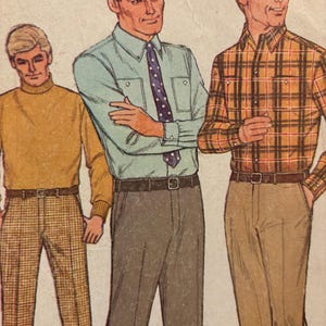 Op de afbeelding: Drie herenmode-illustraties die verschillende shirt- en broekcombinaties laten zien. De man links draagt een bruine trui met een hoge hals en een bruin-witte geruite broek. De man in het midden draagt een lichtblauw overhemd met knopen en een donkerblauw-witte geblokte stropdas en een bruine broek. De man rechts draagt een bruin-wit geruit overhemd en een bruine broek.