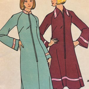 Könnte beinhalten: Zwei Damenkleider mit langen Ärmeln und einem Reißverschluss vorne. Das Kleid links ist hellblau mit einem floralen Besatz. Das Kleid rechts ist burgunderrot mit einem rosa Besatz.