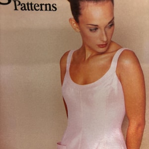 May include: A light pink dress with a scoop neckline and two front pockets. The dress has a fitted bodice and a straight skirt. The Vogue Patterns logo is visible in the upper left corner.