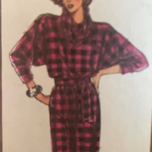 Può includere: Una tuta a quadri neri e rosa con maniche lunghe e una cintura da annodare in vita.