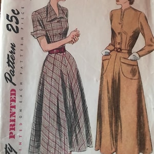 May include: Vintage Simplicity pattern 2617 showing illustrations of two dresses. One is a plaid print with a red belt, the other is a solid tan colour with a matching hat. The pattern includes size 14 and bust 32.