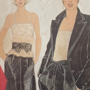 May include: Two women wearing black trousers with a white top and a black belt. One woman is wearing a black blazer.