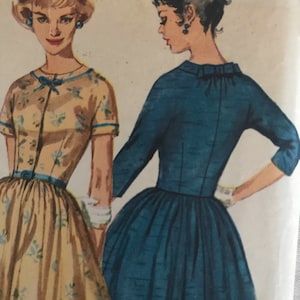 May include: Two vintage sewing patterns for dresses. The dress on the left is a light yellow with a floral print and a bow at the neckline. The dress on the right is a dark blue with a bow at the neckline.