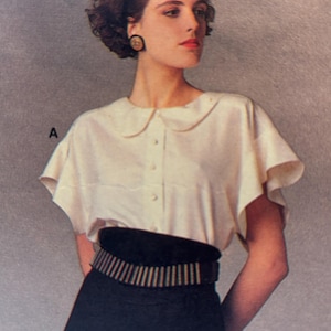 May include: A vintage fashion image featuring a woman wearing a cream-colored blouse with a Peter Pan collar and short, flared sleeves. She is wearing a black skirt and a wide black belt with a striped design. The image has a retro aesthetic.