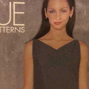 May include: A dark grey sleeveless dress with a V-neck. The image shows a woman with long, dark hair. The words "UE" and "TTERNS" are visible in white text. The background is a neutral colour.