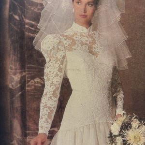Peut inclure: Robe de mariée ivoire vintage avec un col montant et des manches longues en dentelle. La robe présente un corsage ajusté et une jupe à volants. Un voile transparent et un bouquet de fleurs blanches complètent le look.