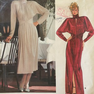 May include: Vogue Patterns American Designer sewing pattern #1478 by John Anthony. The pattern includes two dress designs, one in a light beige color and the other in a deep red color. Both dresses feature a high neck and long sleeves.